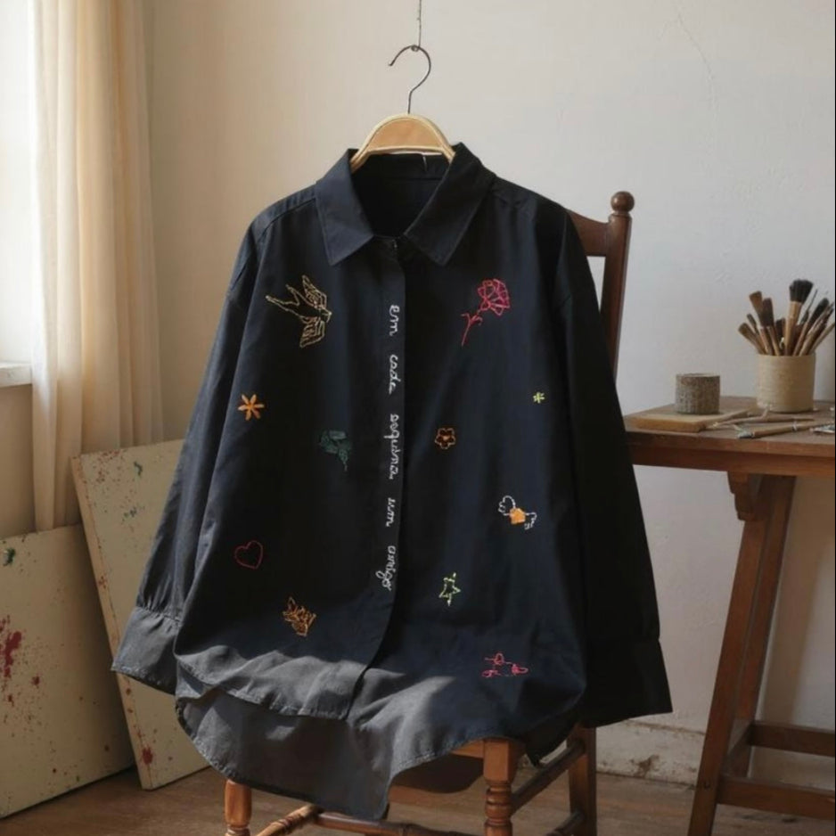 Black embroidered shirt on a wooden chair in a room with a window and art supplies.